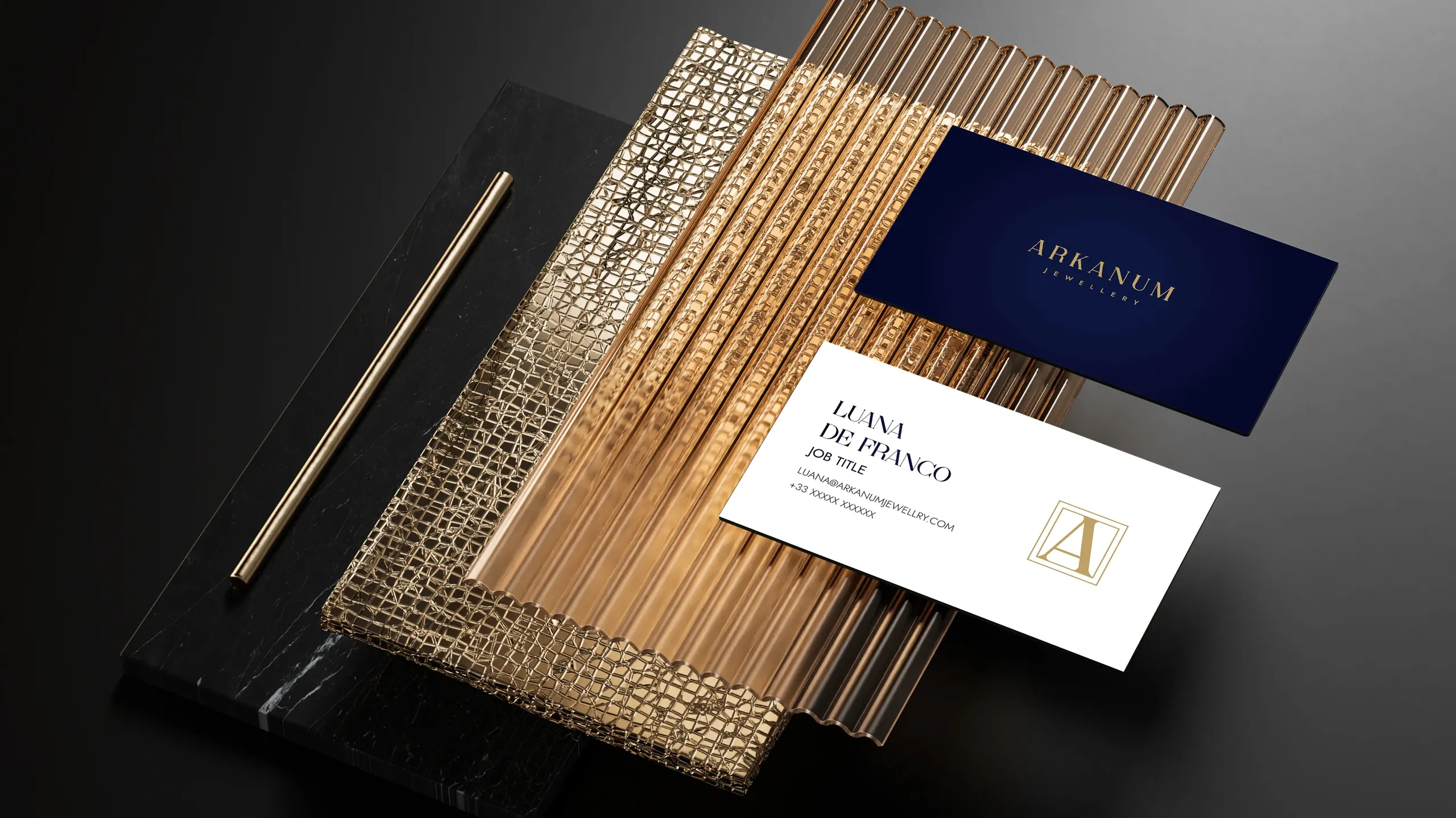 Two luxury business cards for Arkanum Jewellery placed on layered textured gold and black surfaces with a gold pen beside them.